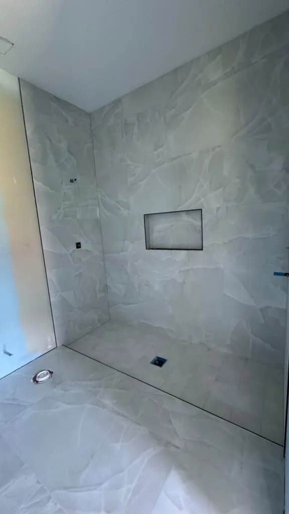 Curbless walk-in shower in large gray marble-look tile with a black-framed niche