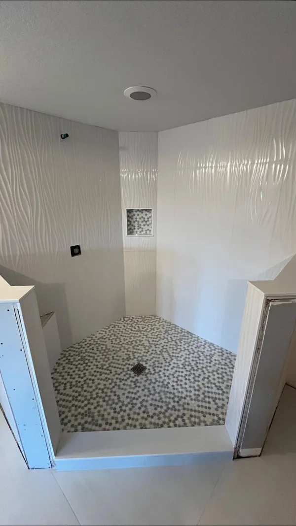 White textured-tile shower with a pebble mosaic floor and a half wall