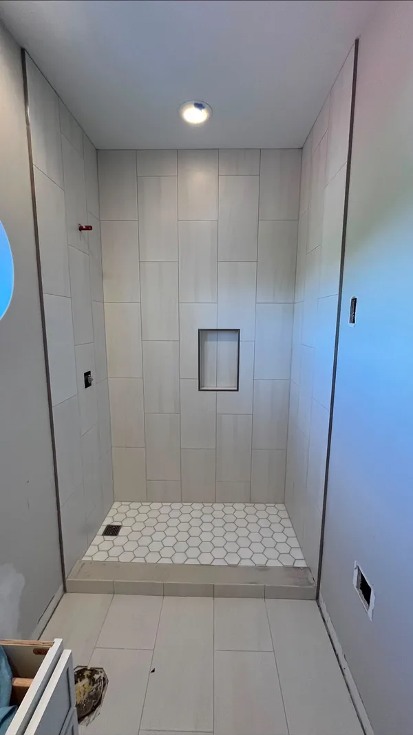 Vertical white tile shower with a recessed niche and hexagon floor