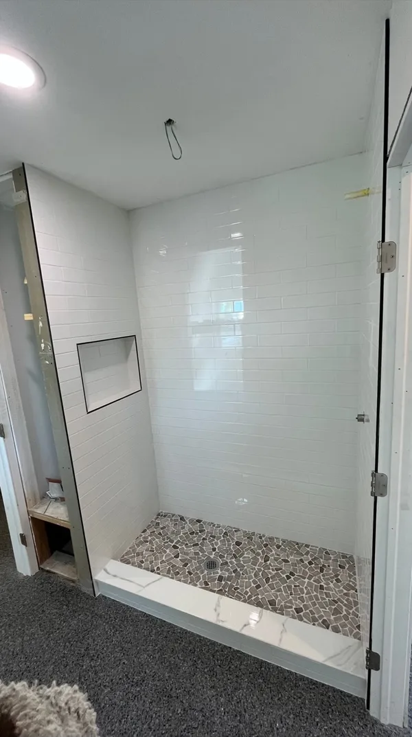White tile shower with a glass panel, recessed niche, and pebble mosaic floor